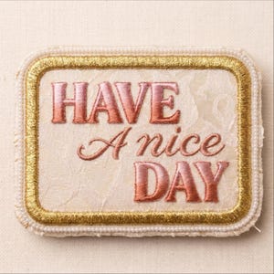 May include: A rectangular embroidered patch featuring the text HAVE A nice DAY in a gradient pink to orange thread. The patch has a cream-colored textured fabric background, a metallic gold embroidered border, and a white beaded outer edge.