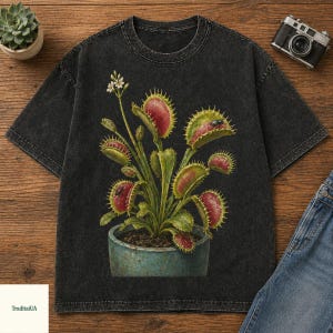 May include: Dark gray t-shirt featuring a detailed illustration of a Venus flytrap plant in a blue pot. The plant has red and green leaves and small white flowers. The shirt has a vintage, washed look.