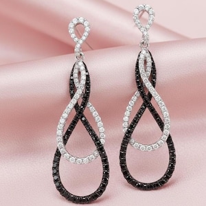 May include: A pair of dangle earrings with a silver-toned top and a black and white intertwined teardrop design. The teardrops are adorned with black and white gemstones, creating a striking contrast. The earrings are designed to dangle and catch the light.