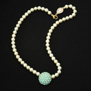 May include: A necklace featuring a strand of white pearls with a central spherical pendant covered in small turquoise beads and gold accents. The necklace includes a gold-toned lobster clasp and a teardrop-shaped pearl charm at the closure.
