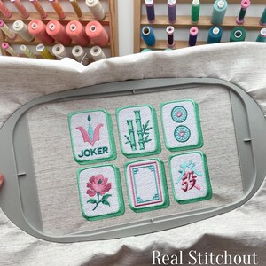 Close up real stitchout of machine embroidered mahjong tile designs showing satin stitch border and thread texture.