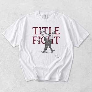 Puede incluir: Camiseta blanca con un gr&aacute;fico burdeos. El gr&aacute;fico muestra las palabras "TITLE FIGHT" sobre una imagen en blanco y negro de dos personas. El texto "the lost year" est&aacute; debajo.