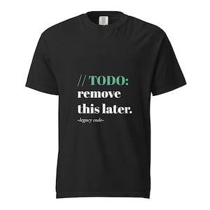 Puede incluir: Camiseta negra con el texto "//TODO: remove this later. -legacy code-" en blanco y verde. La camiseta tiene cuello redondo y mangas cortas. El texto está centrado en la parte delantera de la camiseta.
