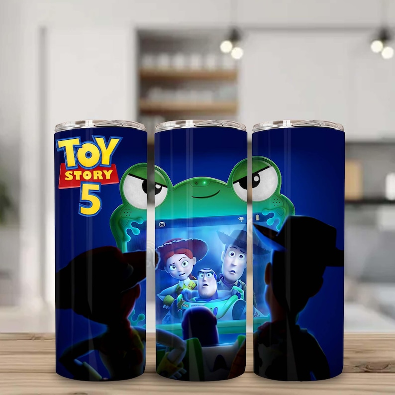 May include: A cylindrical tumbler featuring a dark blue background with the Toy Story 5 logo in yellow and red. The design displays a green alien character at the top and a screen showing Jessie, Woody, and Buzz Lightyear in the center.