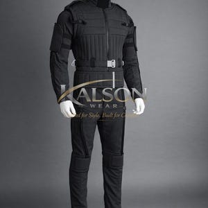 May include: Black tactical jumpsuit displayed on a mannequin. The jumpsuit features a quilted design on the chest and upper arms, with reinforced padding on the knees and elbows. It includes a belt with a silver buckle and the "KALSON WEAR" logo.