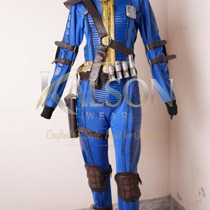 May include: A blue jumpsuit with yellow trim and the number 33 on the collar. It features brown leather-like straps, a belt with small canisters, dark brown knee and shin guards, and a shoulder piece, displayed on a black mannequin.