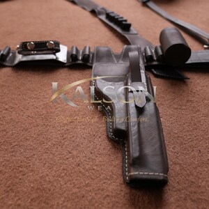 May include: A dark brown leather holster with white stitching, part of a belt set. The set includes a belt with multiple pouches, a cylindrical object, and a buckle. The image is on a brown surface.