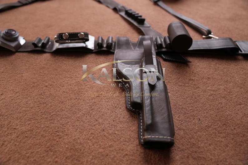 May include: A dark brown leather holster with white stitching, part of a belt set. The set includes a belt with multiple pouches, a cylindrical object, and a buckle. The image is on a brown surface.
