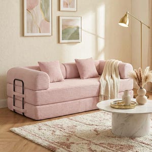 May include: A pink corduroy sofa with matching pillows and a cream-colored throw blanket. The sofa is in a living room setting with abstract art, a marble coffee table, and a gold floor lamp. The rug has a pink and cream pattern.