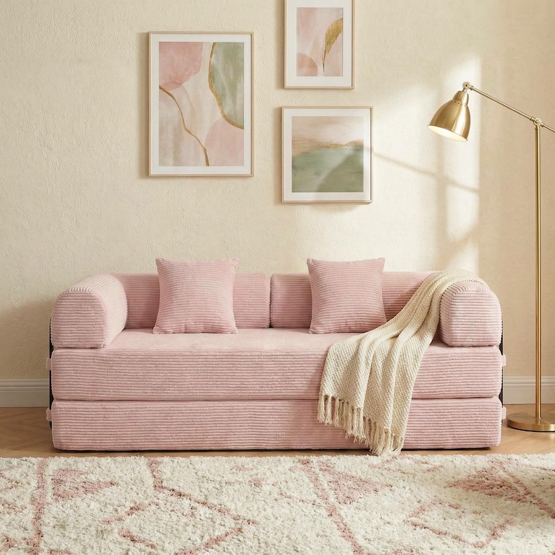 Puede incluir: Un sof&aacute; rosa de pana con dos cojines cuadrados a juego y una manta crema. El sof&aacute; est&aacute; frente a una pared con tres obras de arte abstractas enmarcadas y una l&aacute;mpara de pie dorada. El sof&aacute; mide aproximadamente 180 cm de largo.