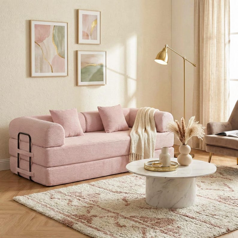 May include: A pink corduroy sofa with matching pillows and a cream-colored throw blanket. The sofa is in a living room setting with abstract art, a marble coffee table, and a gold floor lamp. The rug has a pink and cream pattern.