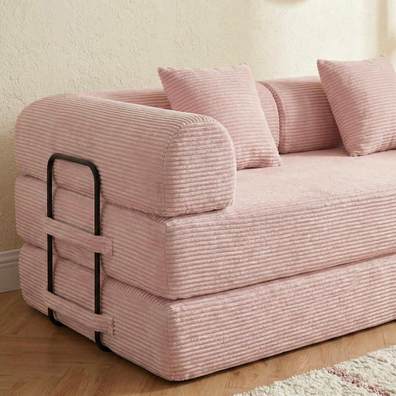 Puede incluir: Un sof&aacute; de pana rosa con estructura met&aacute;lica negra. El sof&aacute; tiene un reposabrazos redondeado y tres cojines a juego. La tela de pana tiene una textura acanalada. El sof&aacute; es de color rosa claro.