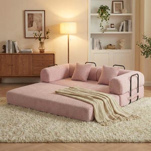 Puede incluir: Un sof&aacute; modular de pana rosa con detalles met&aacute;licos negros y cojines a juego. Una manta beige con flecos descansa sobre el sof&aacute;. El sof&aacute; est&aacute; sobre una alfombra de pelo largo color crema, creando un espacio habitable acogedor.