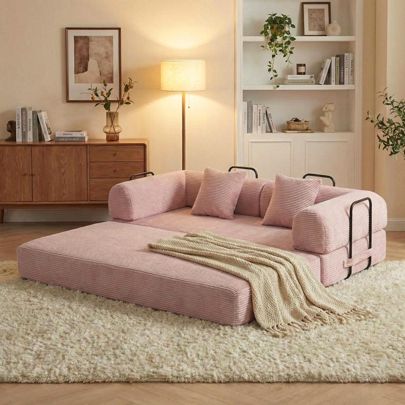 Puede incluir: Un sof&aacute; modular de pana rosa con detalles met&aacute;licos negros y cojines a juego. Una manta beige con flecos descansa sobre el sof&aacute;. El sof&aacute; est&aacute; sobre una alfombra de pelo largo color crema, creando un espacio habitable acogedor.