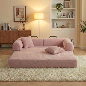 Puede incluir: Un sof&aacute; de pana rosa con dos cojines a juego y una base grande y plana. El sof&aacute; est&aacute; sobre una alfombra de pelo crema. El sof&aacute; tiene reposabrazos de metal negro y est&aacute; en una habitaci&oacute;n bien iluminada.