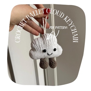 Puede incluir: Un llavero de nube tejido a ganchillo, con una cara sonriente y pequeñas piernas marrones. El llavero es blanco y tiene el texto "CROCHET BALLET CLOUD KEYCHAIN" y "PDF PATTERN". Se sujeta con una cuerda blanca.