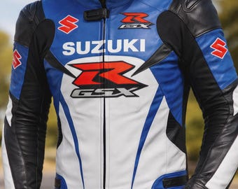 May include: A blue, white, and black leather motorcycle jacket with the Suzuki and GSX logos prominently displayed. The jacket features a stand-up collar, zippered front, and black leather accents on the sleeves and shoulders. The jacket is designed for motorcycle riding.