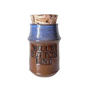 May include: A cylindrical ceramic jar with a cork stopper. The upper section is glazed in a speckled blue, while the lower body is a textured brown. The words BELLY BUTTON LINT are embossed in capital letters on the front of the brown section.
