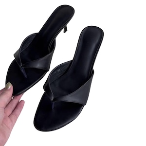 May include: A pair of black leather thong sandals with a small heel. The sandals have a minimalist design, featuring a toe post and a strap that wraps around the foot. The heels are approximately 2 inches high.