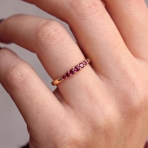 Op de afbeelding: Een gouden ring met een rij van vijf kleine, ronde, dieproze edelstenen die in een lijn aan de bovenkant zijn gezet. Het metaal heeft een gepolijste afwerking en de stenen zijn gelijkmatig verdeeld, wat zorgt voor een verfijnde uitstraling.