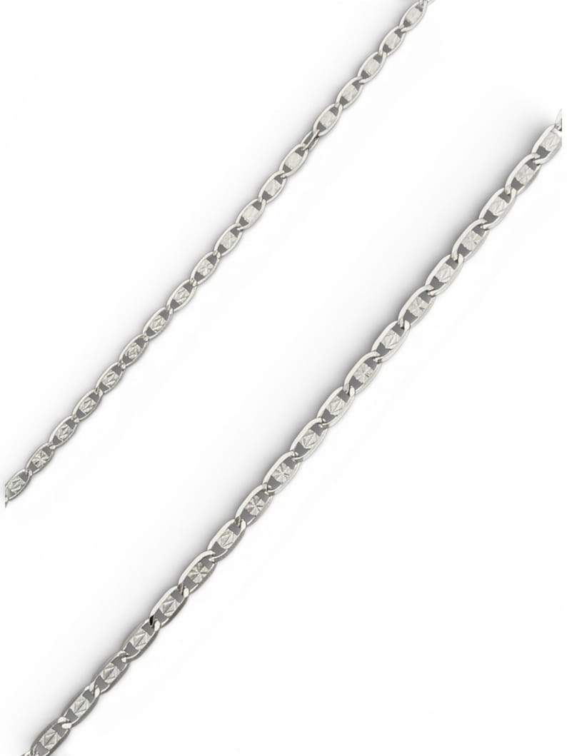 May include: A silver-colored chain necklace with a repeating oval and diamond-shaped pattern. The chain is displayed against a white background, highlighting its reflective surface and intricate design. The necklace appears to be made of metal.