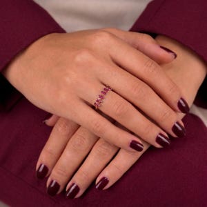 Pode incluir: Um anel de ouro com uma série de pequenas pedras preciosas cor-de-rosa em corte marquise, dispostas num delicado padrão de folha ao longo da banda. O anel é usado num dedo, exibindo as vibrantes pedras cor-de-rosa no metal dourado polido.