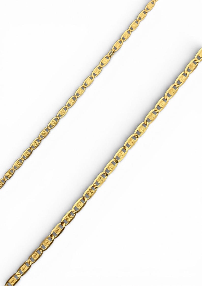 May include: Two gold-colored necklaces with a repeating oval and starburst design. The chains are displayed diagonally against a white background. The jewelry is likely made of metal and is suitable for wearing.