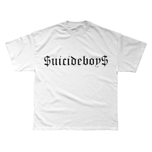 May include: White t-shirt featuring the text "Suicideboys$" in a gothic font. The text is centrally placed. The shirt has a crew neck and short sleeves.