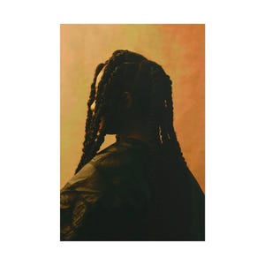 May include: A side profile of a person with long, dark, braided hair. The person is wearing a dark-colored top. The background is a gradient of orange and yellow.