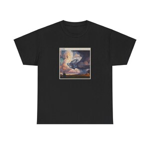 May include: Black t-shirt featuring a square graphic with the text "MILLERS" and "Something for the World". The graphic depicts a surreal scene with clouds, a hand, and a landscape. The shirt is made of a soft material.