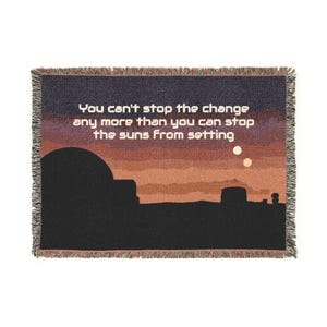 Peut inclure: Plaid tissé avec un motif de coucher de soleil dans les tons orange, marron et violet. La couverture présente une silhouette de paysage et le texte "You can't stop the change any more than you can stop the suns from setting."