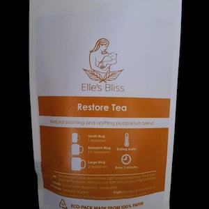 May include: A white pouch of Elle's Bliss Restore Tea. The packaging features a logo of a woman holding a baby. The label includes instructions for brewing, with measurements in teaspoons. The text reads "Natural soothing and uplifting postpartum blend."