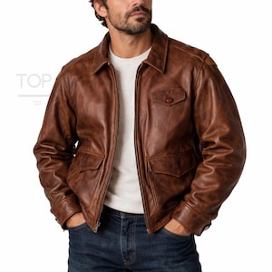 Può includere: Giacca in pelle marrone con collo, due tasche frontali e chiusura con zip. La giacca ha un design classico e un aspetto vintage. L'immagine mostra anche il testo "TOP" e "SINCE 2012".