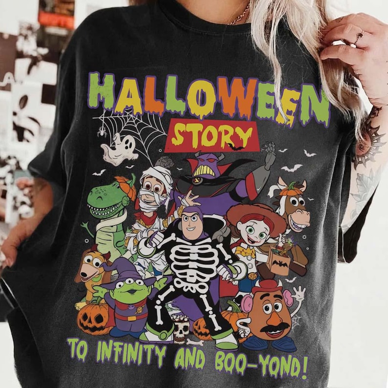 May include: Dark grey t-shirt with a Halloween-themed design. The graphic includes the words "HALLOWEEN STORY" and "TO INFINITY AND BOO-YOND!". Cartoon characters are depicted in Halloween costumes, including a mummy, a skeleton, and a dinosaur.