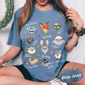 May include: Blue jean Comfort Colors t-shirt featuring cartoon character portraits from a movie. Characters include Nick Wilde, Judy Hopps, and Flash. The shirt has the text "Comfort Colors Blue Jean".