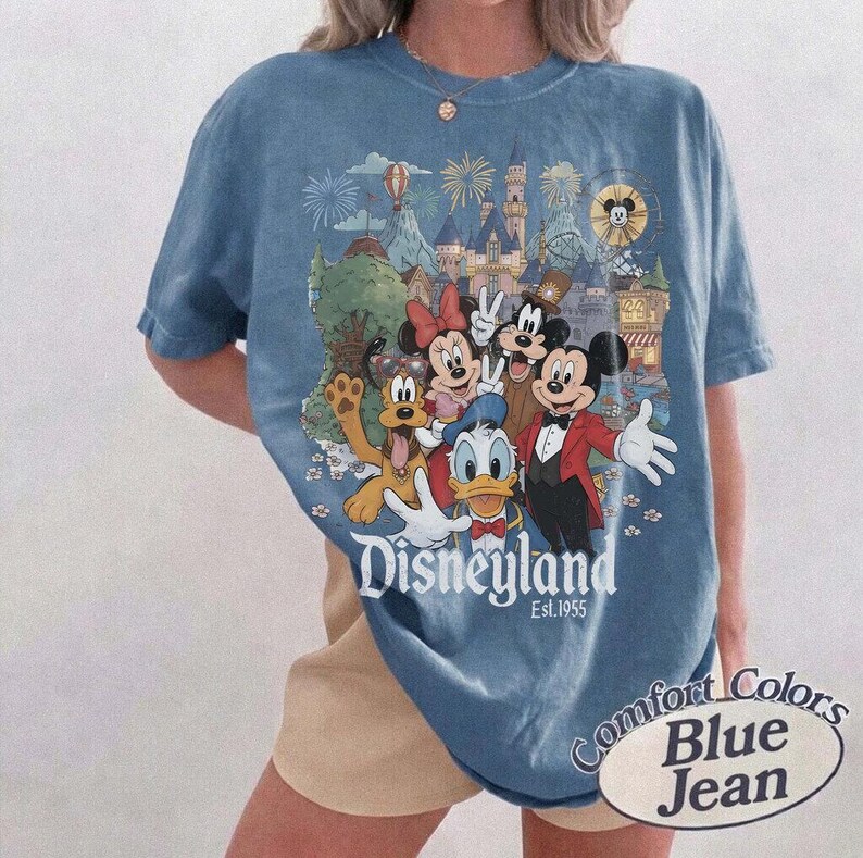 Pu&ograve; includere: Una t-shirt color blu jeans con una stampa grafica di Topolino, Minnie, Paperino, Pippo e Pluto davanti a un castello. Il testo Disneyland Est. 1955 &egrave; stampato sotto i personaggi. La maglietta presenta un girocollo.