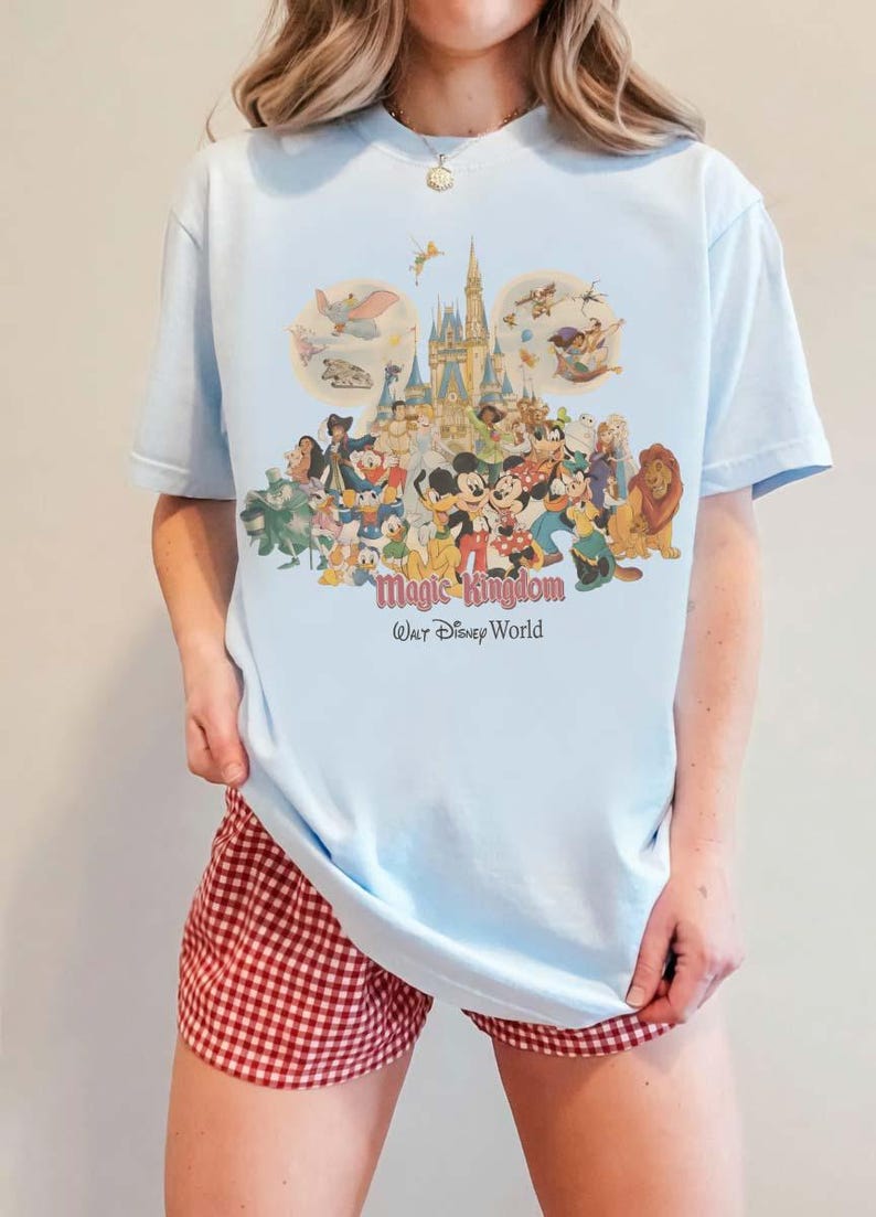 May include: Light blue t-shirt featuring a colorful graphic of Disney characters, including Mickey Mouse, Donald Duck, and Cinderella's castle. The text "Magic Kingdom Walt Disney World" is printed below the graphic.