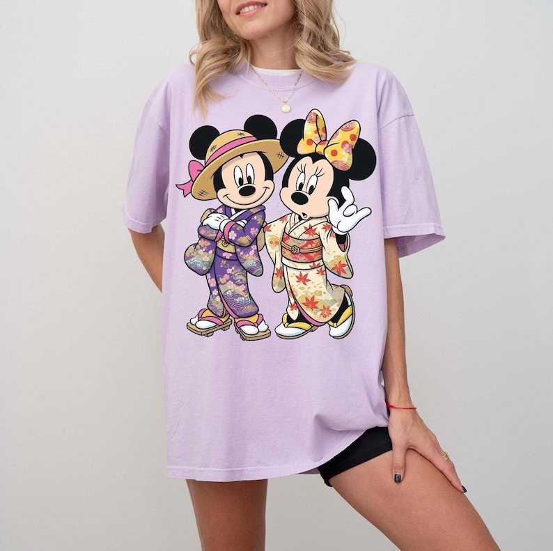 Puede incluir: Camiseta lila con un dise&ntilde;o de Mickey y Minnie Mouse con atuendos japoneses. Mickey lleva un sombrero de paja y un kimono morado, Minnie un lazo amarillo y un kimono con estampados florales. El dise&ntilde;o est&aacute; centrado en la camiseta.