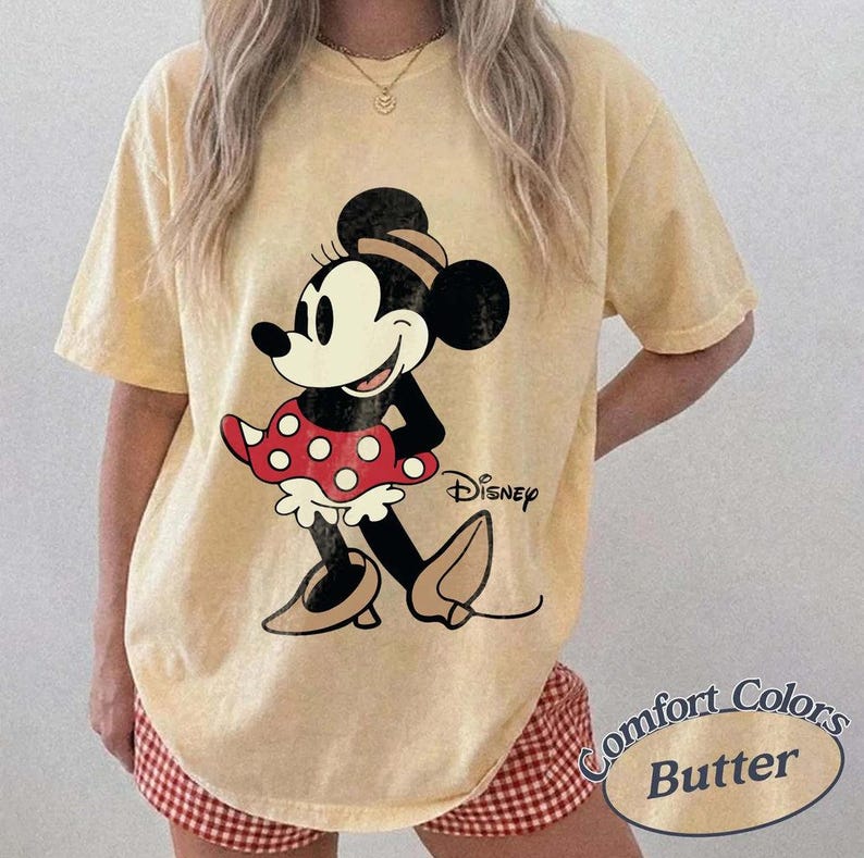 May include: Yellow t-shirt featuring a Minnie Mouse graphic. The cartoon character is depicted in black, white, and red, with the Disney logo. The shirt is labeled "Comfort Colors Butter".