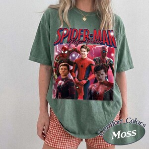 May include: Green t-shirt featuring a graphic of Spider-Man and the text "Spider-Man Peter Parker". The graphic includes images of Spider-Man in various poses. The shirt also has the text "Comfort Colors Moss".
