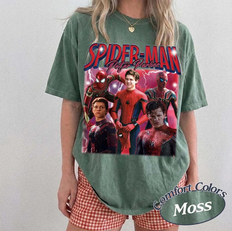 May include: Green t-shirt featuring a graphic of Spider-Man and the text "Spider-Man Peter Parker". The graphic includes images of Spider-Man in various poses. The shirt also has the text "Comfort Colors Moss".