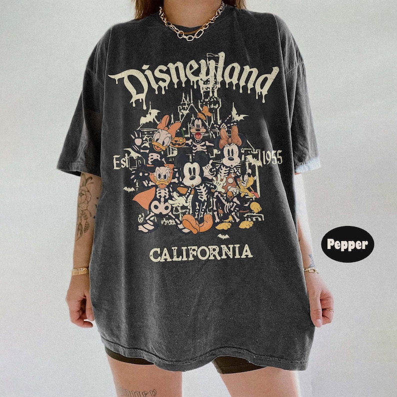 May include: Dark gray t-shirt featuring a Disneyland graphic with Mickey Mouse and friends in Halloween costumes. The shirt has the text "Disneyland California Est. 1955" in a distressed font. The shirt is oversized.