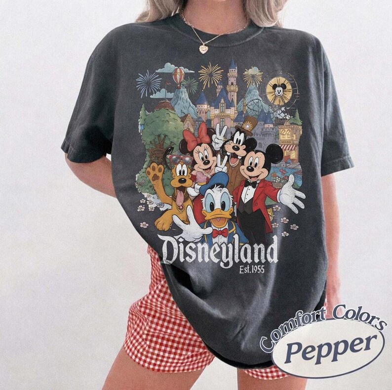 Pu&ograve; includere: Una t-shirt grigio antracite a maniche corte con una grafica colorata di Topolino, Minni, Paperino, Pippo e Pluto davanti a un castello con fuochi d'artificio. Il testo Disneyland Est. 1955 &egrave; stampato in bianco sotto i personaggi.