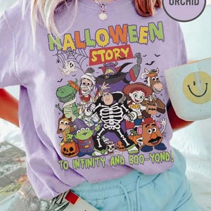 May include: A lilac t-shirt with a Halloween graphic featuring cartoon characters. The text "HALLOWEEN STORY" is above the characters, and "TO INFINITY AND BOO-YOND!" is below. The shirt is a casual style, suitable for everyday wear.