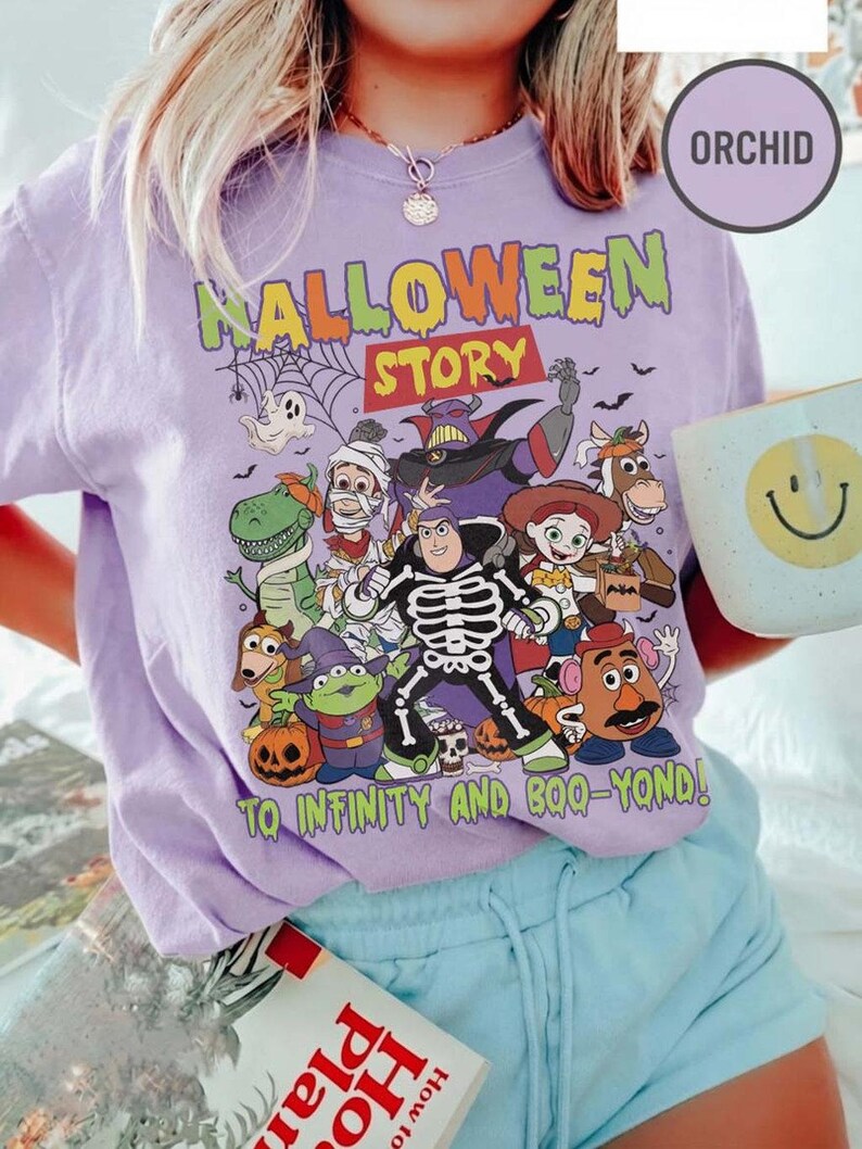 May include: A lilac t-shirt with a Halloween graphic featuring cartoon characters. The text "HALLOWEEN STORY" is above the characters, and "TO INFINITY AND BOO-YOND!" is below. The shirt is a casual style, suitable for everyday wear.