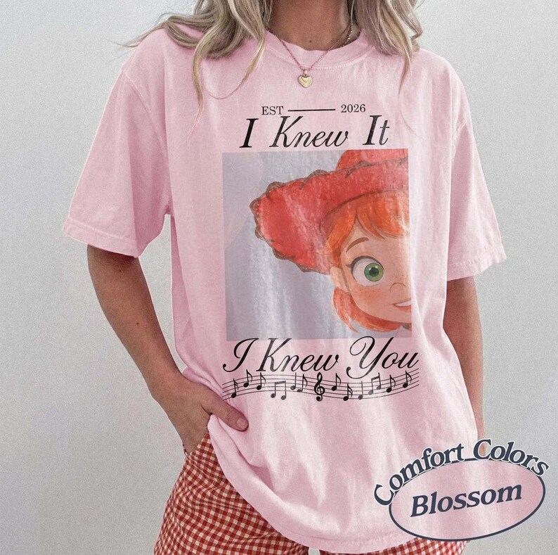 Peut inclure: Un t-shirt rose clair &agrave; manches courtes avec l'illustration d'un personnage de dessin anim&eacute; aux cheveux roux portant un chapeau rouge. Le texte indique EST 2026, I Knew It, et I Knew You, avec une port&eacute;e musicale et des notes sous l'image.