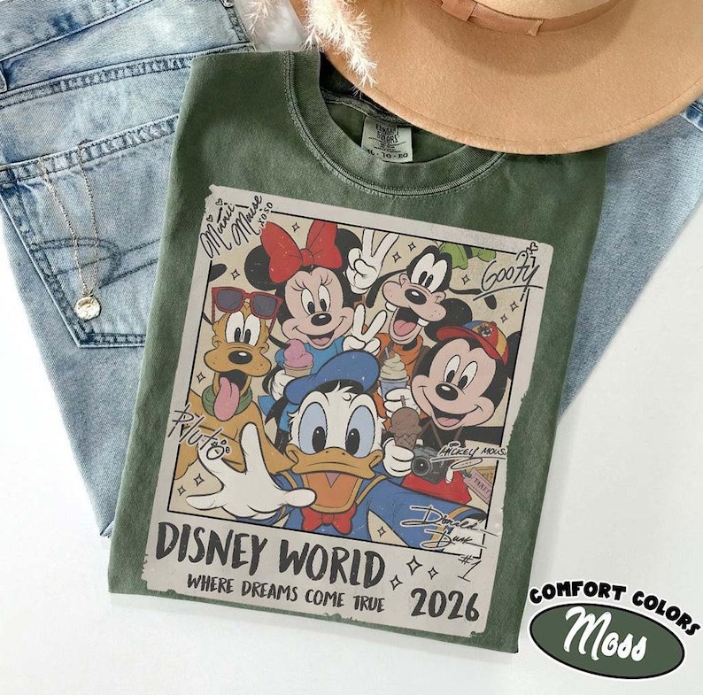 May include: A green Comfort Colors t-shirt featuring a graphic of Disney characters, including Mickey Mouse, Minnie Mouse, Donald Duck, and Goofy. The graphic reads "Disney World Where Dreams Come True 2026". The shirt is paired with blue jeans and a tan hat.