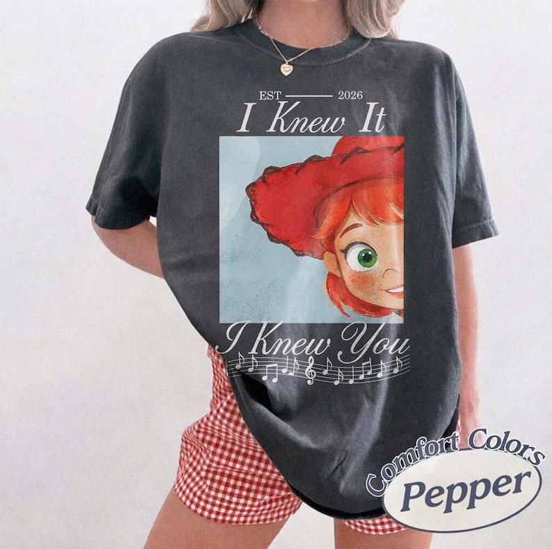 Peut inclure: Un t-shirt gris anthracite &agrave; manches courtes avec un graphique repr&eacute;sentant un personnage au chapeau rouge et aux yeux verts. Le texte indique EST 2026 I Knew It I Knew You, accompagn&eacute; d'une port&eacute;e musicale et de notes. Col rond et coupe d&eacute;contract&eacute;e.
