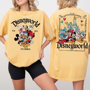 May include: Yellow t-shirt with a Disneyworld graphic on the front and back. The front graphic features Mickey Mouse, Minnie Mouse, Donald Duck, Daisy Duck, Goofy, and Pluto. The back graphic shows the Disney castle and more characters. The text "Disneyworld" and "Florida" are also visible.