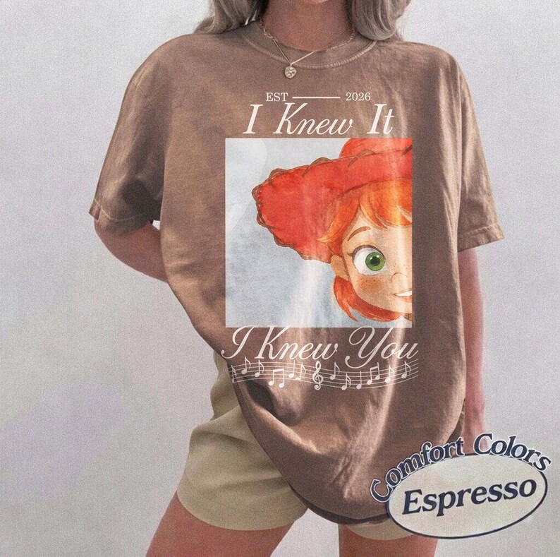 Peut inclure: Un t-shirt marron &agrave; manches courtes avec un graphique repr&eacute;sentant un personnage aux cheveux roux portant un chapeau rouge. Le texte indique "EST 2026 I Knew It I Knew You" avec des notes de musique. Le t-shirt a un col rond et une coupe d&eacute;contract&eacute;e.
